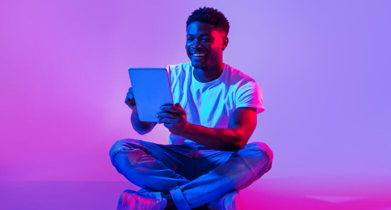 handsome-black-guy-using-tablet-computer-sitting-cross-legged-neon-light-780x420